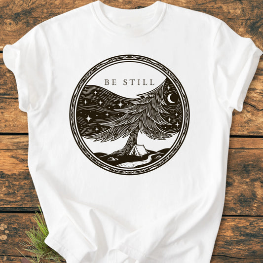 1411 Be Still t-shirt features a central circular print with a stylized pine tree, starry night sky, and 'BE STILL' text, on a soft, durable, ring-spun cotton fabric.