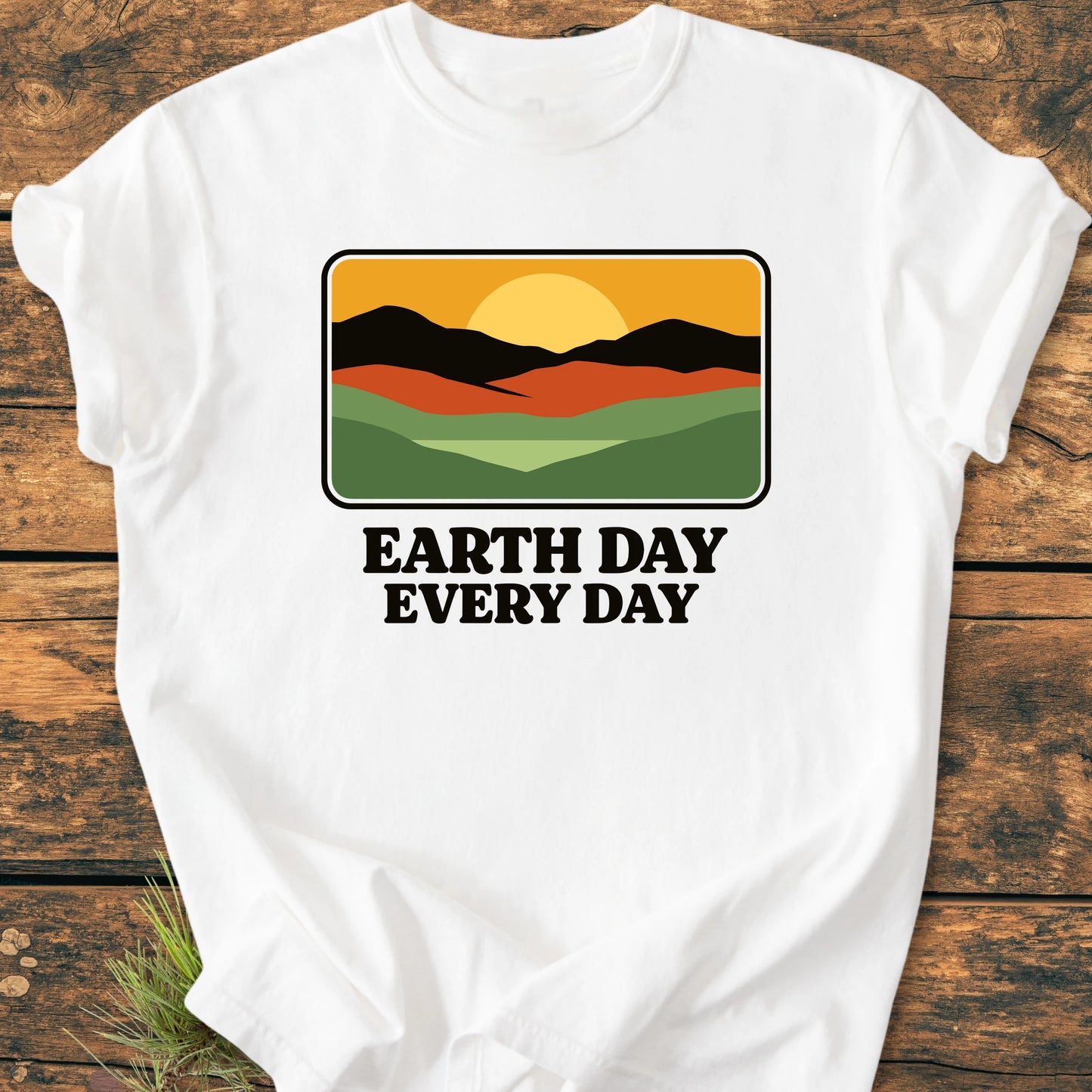 White T-shirt featuring a retro-style graphic of hills and sun with EARTH DAY EVERY DAY text, laid on wood. Vintage wash for a soft, relaxed unisex fit.