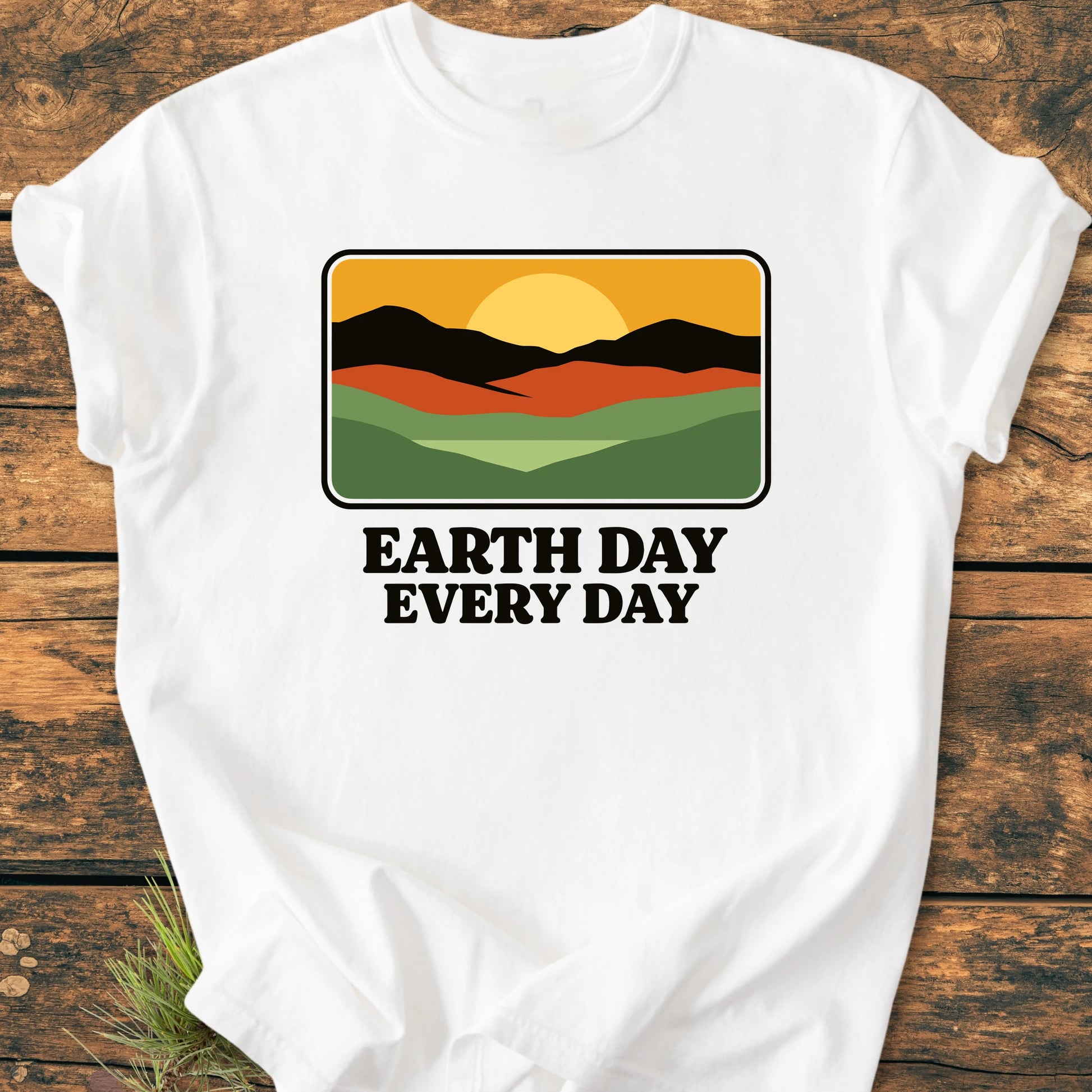 White T-shirt featuring a retro-style graphic of hills and sun with EARTH DAY EVERY DAY text, laid on wood. Vintage wash for a soft, relaxed unisex fit.