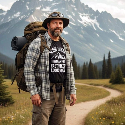 Man hiking in a meadow wearing the Slow Hikers T-Shirt, showcasing its soft, lightweight cotton material and unisex fit, ideal for outdoor adventures.