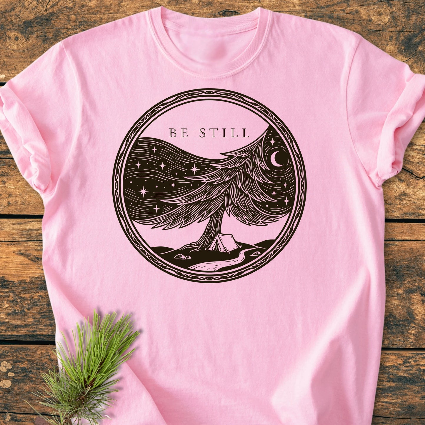 Light pink Be Still T-shirt featuring a serene graphic of a camp scene beneath a starry night sky, encouraging tranquility. Made from soft, ring-spun cotton for daily comfort and durability.