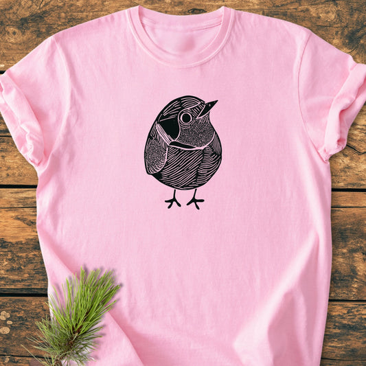 Light pink 1433 Little Robin T-shirt with a black line-art bird illustration, displayed on wood. The vintage wash tee showcases a relaxed fit, perfect for everyday wear.