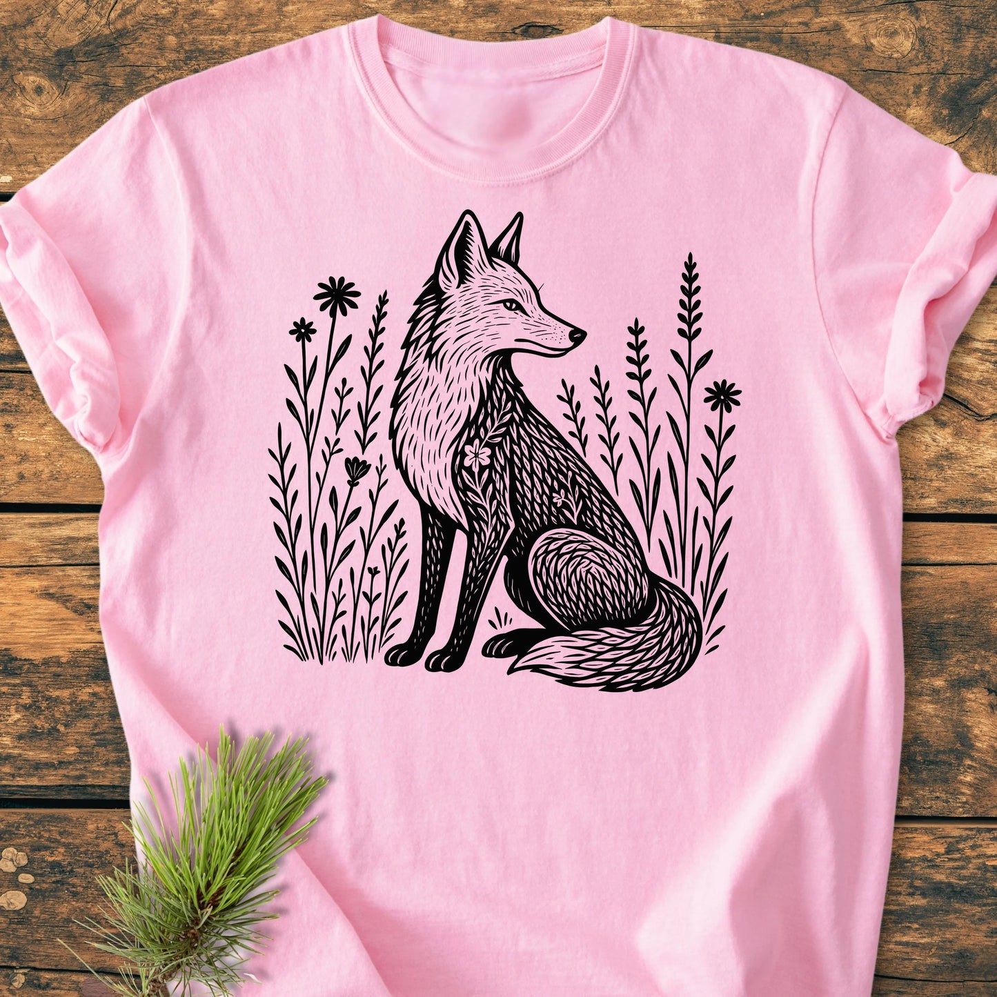 Light pink 225 Wildflower Fox DARK T-shirt featuring a black line-drawing of a fox amid wildflowers, laid on wood. A pine sprig rests beside, highlighting its nature-inspired design.