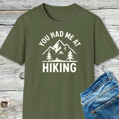 You Had Me At Hiking T-Shirt featuring mountain graphic and slogan, laid on wooden surface. Made of soft cotton, perfect for outdoor enthusiasts.