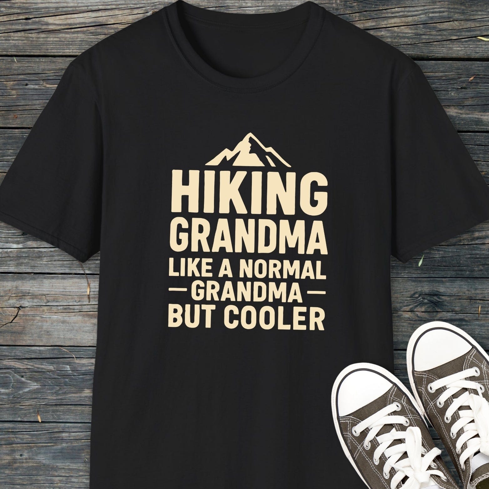 Hiking Grandma T-Shirt with mountain silhouette and slogan, displayed on wood. Features soft ring-spun cotton, pre-shrunk, durable print, and taped shoulders for comfort.