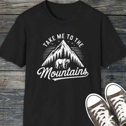Take Me To The Mountains T-Shirt with vintage mountain graphic, pine trees, and bear silhouette, paired with canvas sneakers, highlighting adventure-ready comfort and unisex fit.