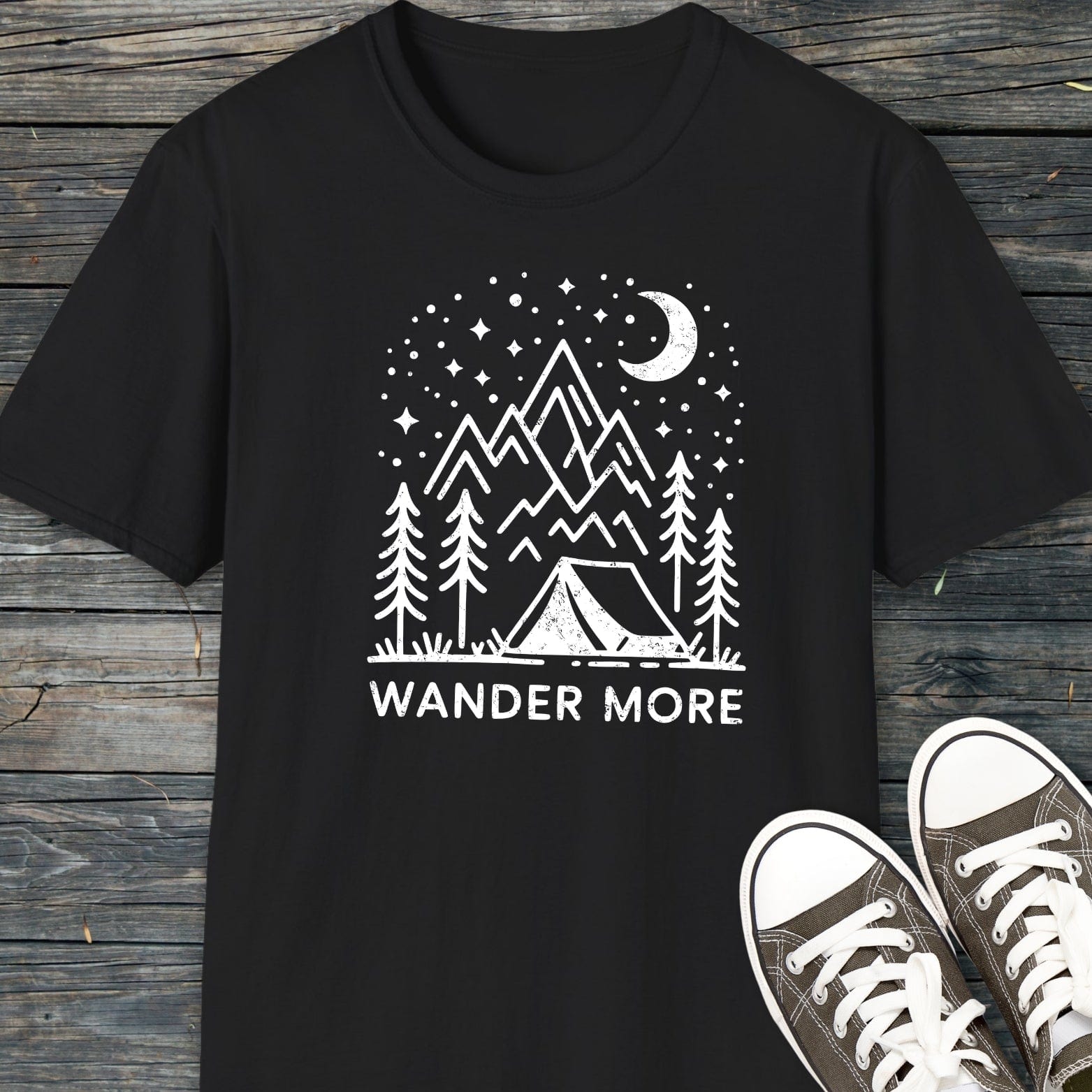 Wander More T-Shirt featuring a hand-drawn camping scene with a tent, trees, and mountains, highlighting outdoor adventure. Paired with canvas sneakers for a complete look.