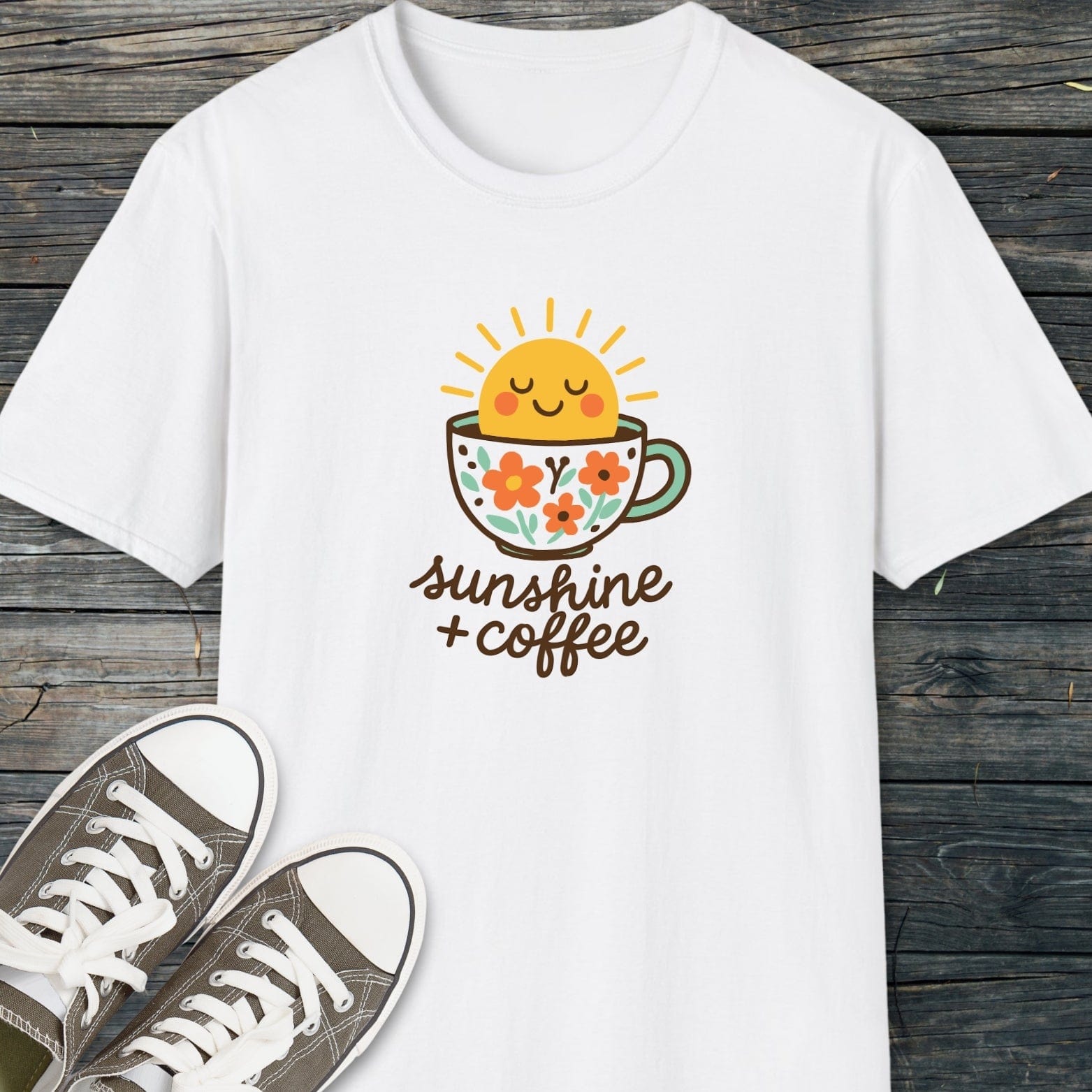 Sunshine And Coffee T-Shirt featuring a smiling sun graphic on a floral cup, laid on wood, with canvas sneakers. Comfortable, unisex, soft cotton for everyday adventures.