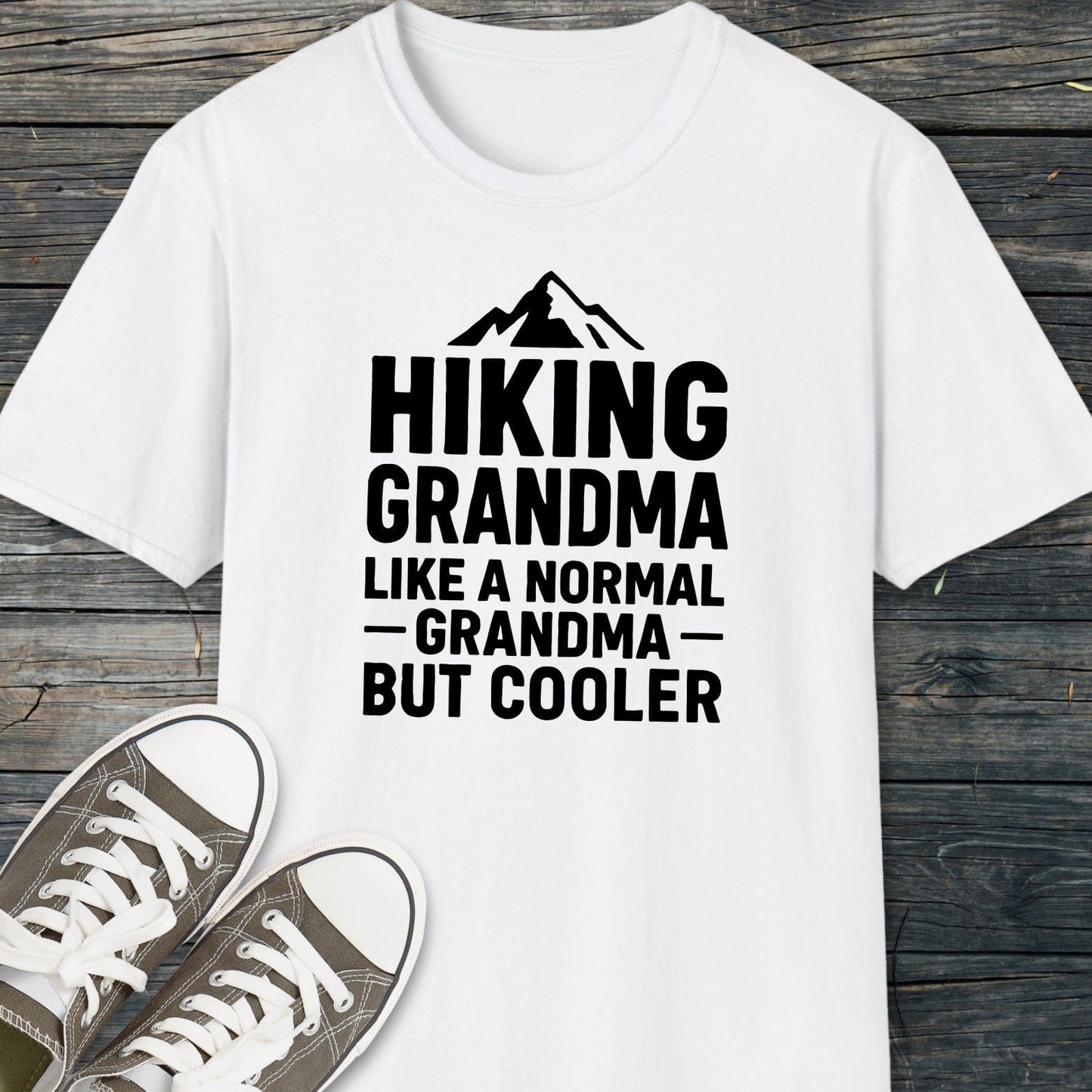 Hiking Grandma T-Shirt with bold text and mountain silhouette, paired with casual canvas sneakers, showcasing everyday adventure and outdoor-inspired style on a wooden surface.