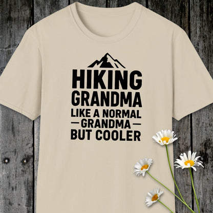Hiking Grandma T-Shirt featuring a bold mountain graphic and text, laid flat with daisies nearby; crafted from lightweight cotton for comfort and durability.