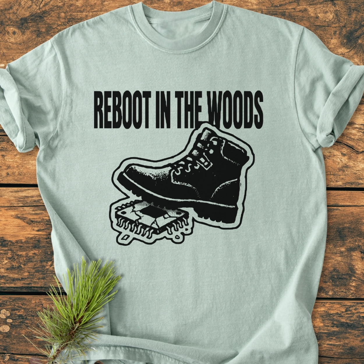 Reboot In The Woods - Vintage Wash Tee featuring a hiking boot on a CPU graphic, spruce branch accent, on rustic wood. Relaxed fit, durable stitching, soft-washed for comfort.
