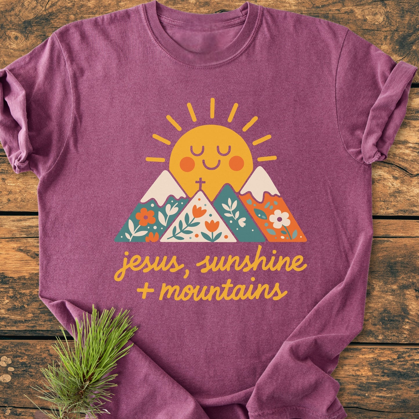 Jesus, Sunshine, Mountains - Vintage Heavyweight Tee featuring a cheerful sun, mountains, and florals graphic, laid on wood with a pine sprig; cozy fit, 100% ring-spun cotton, durable stitching.