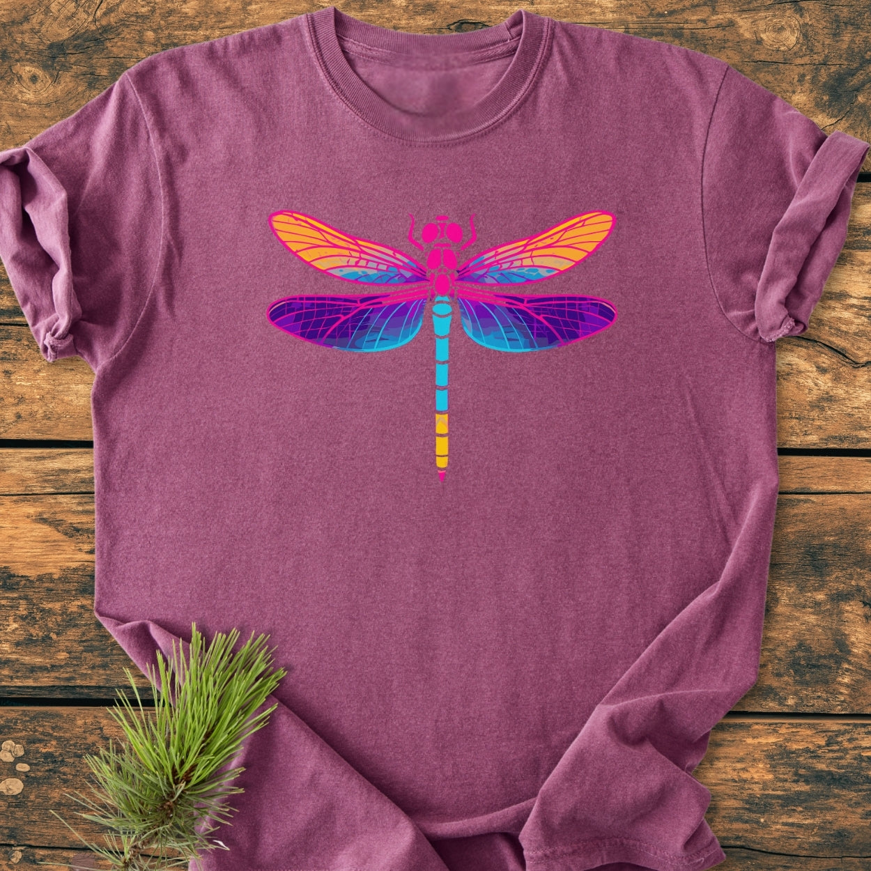 Psychedelic Dragonfly - Vintage Wash Tee in heather purple, featuring a multicolored dragonfly graphic, lies on wood. A pine branch accents the scene, highlighting the T-shirt's soft, relaxed fit.