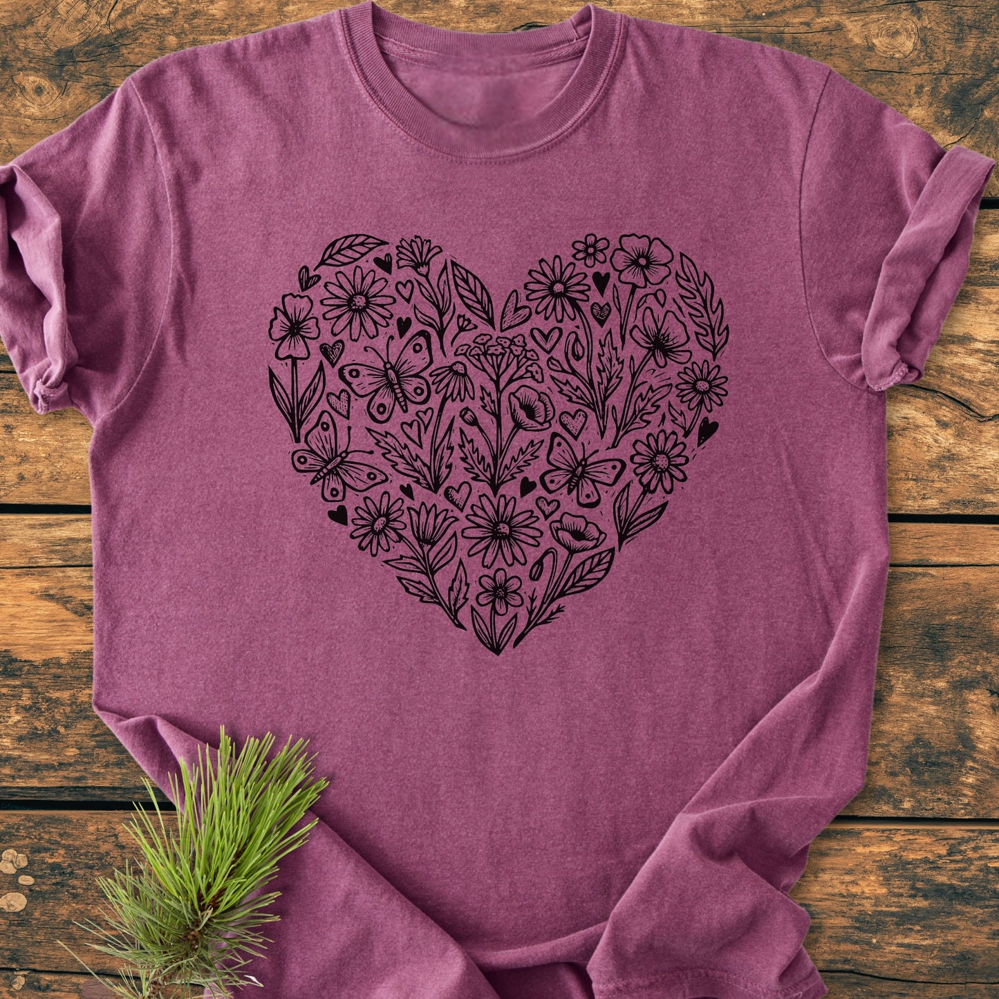 Wildflower Heart Butterfly Soul - Vintage Heavyweight Tee features a black line-art heart with flowers, leaves, and butterflies on a soft, heathered-raspberry T-shirt, laid on a rustic wooden surface.