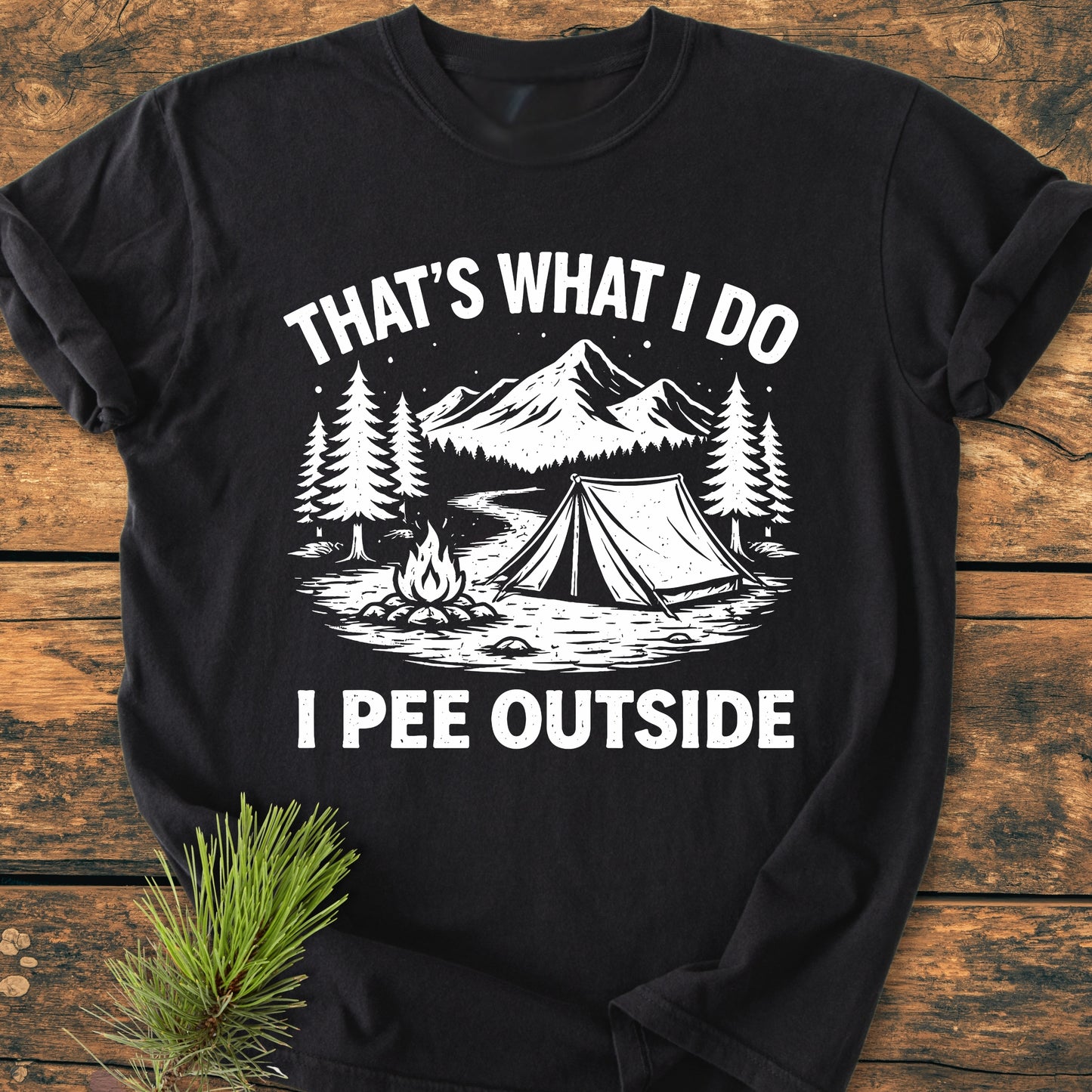 I Pee Outside - Vintage Wash Tee featuring a camping scene with pine trees and mountains on a black T-shirt, showcasing a relaxed fit and durable, soft-washed fabric on a wooden surface.