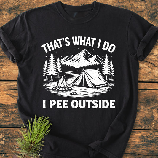 I Pee Outside - Vintage Wash Tee featuring a camping scene with pine trees and mountains on a black T-shirt, showcasing a relaxed fit and durable, soft-washed fabric on a wooden surface.