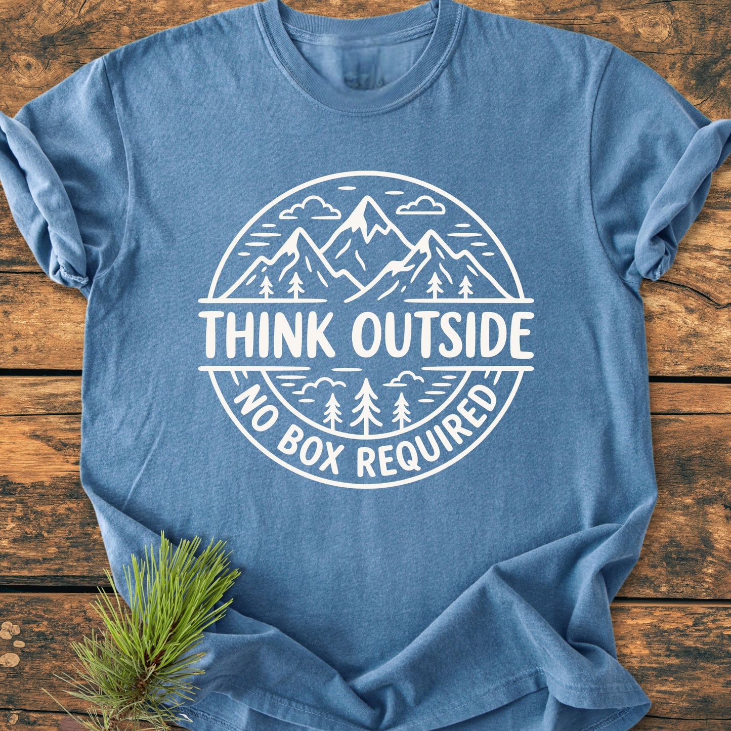 Think Outside - Vintage Wash Tee featuring a white mountain-and-forest design with “THINK OUTSIDE” slogan, laid on wooden surface with a pine branch, highlighting its soft, relaxed fit and durable construction.