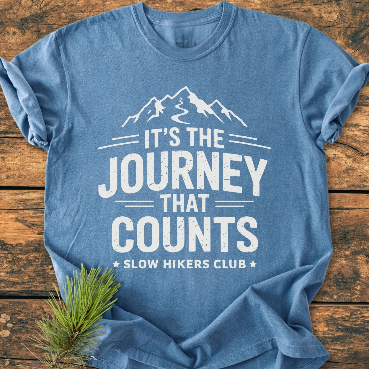Heather-blue It's The Journey That Counts - Vintage Wash Tee with white mountain silhouette and slogan, laid on wood. Features soft-washed fabric, relaxed fit, and durable double-needle stitching.
