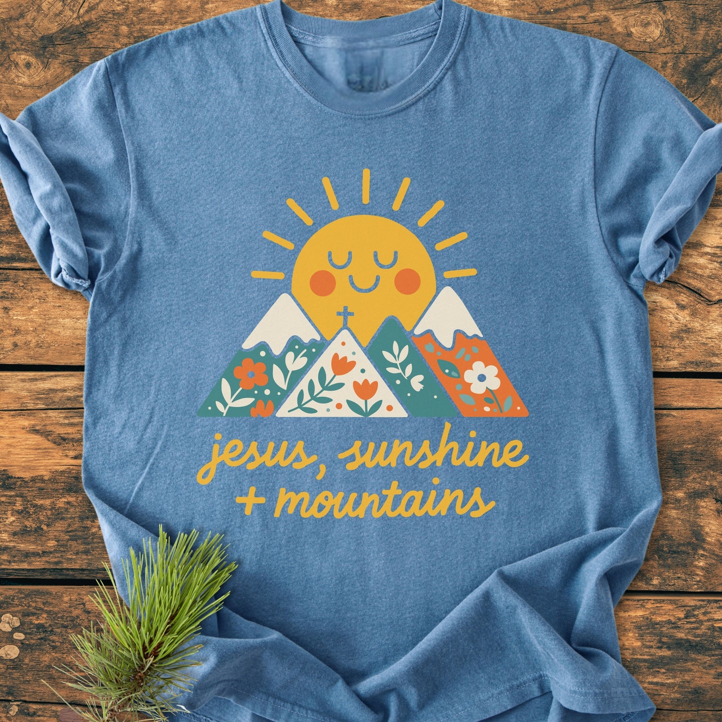 The Jesus, Sunshine, Mountains - Vintage Heavyweight Tee features a smiling sun over floral-patterned mountains with the phrase “jesus, sunshine + mountains” on a heather-blue T-shirt, showcasing comfort and durability.