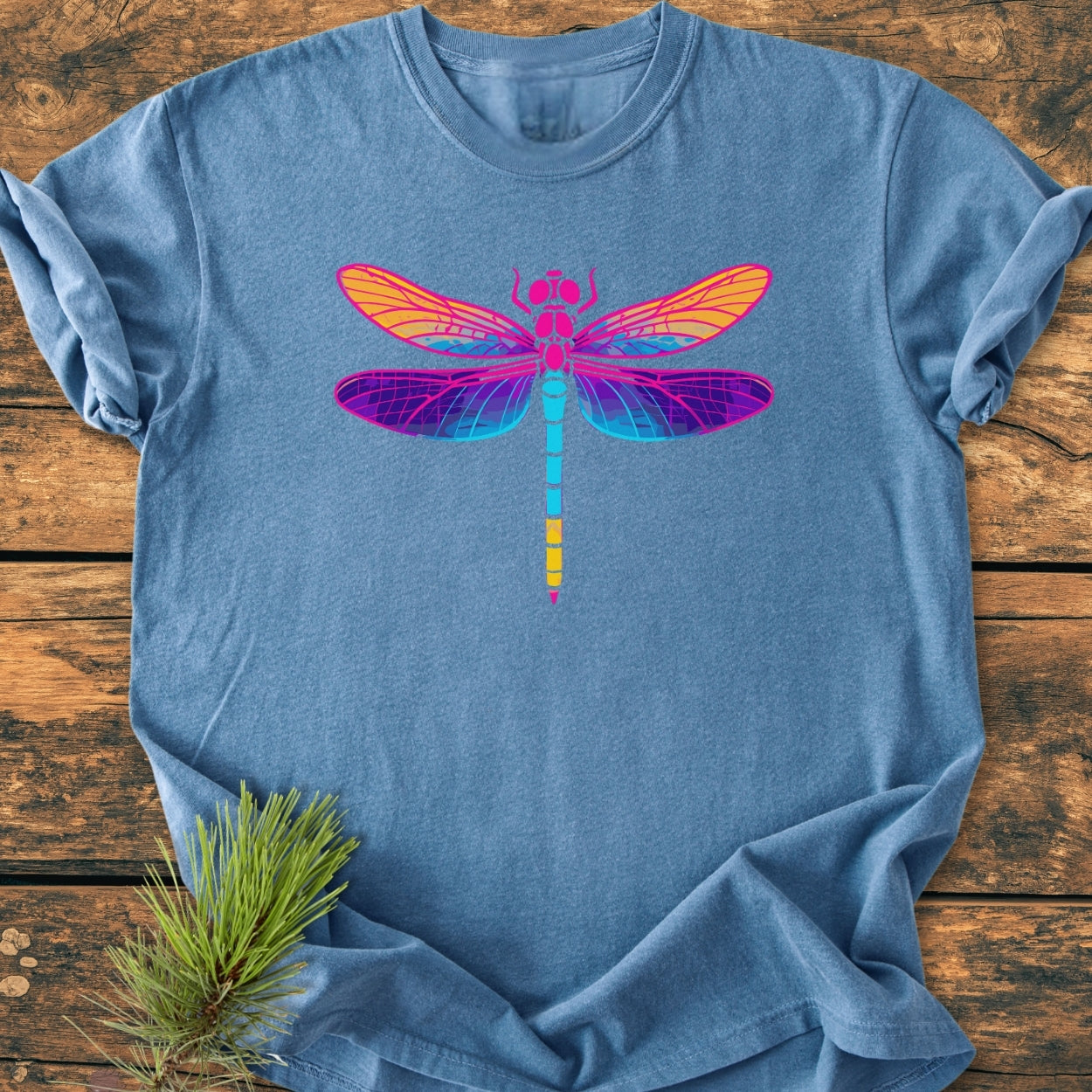 Psychedelic Dragonfly - Vintage Wash Tee displays a vibrant dragonfly graphic on a heather-blue backdrop, highlighting the shirt's relaxed, durable design, laid flat with a pine sprig accent.
