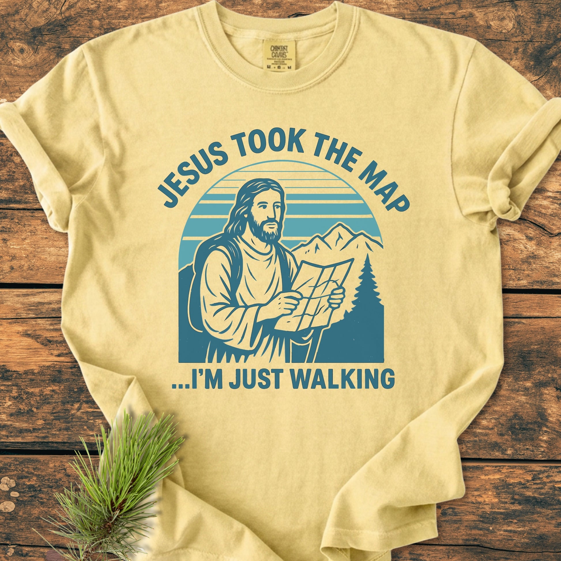 Jesus Took The Map - Vintage Wash Tee features a stylized graphic of Jesus with a backpack and map. Laid flat, it highlights the relaxed fit of the garment-dyed, soft-washed cotton.