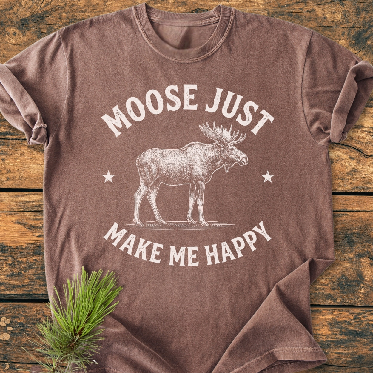 Moose Make Me Happy - Vintage Wash Tee features a white moose illustration with stars on a brown, short-sleeved, garment-dyed tee, laid on rustic wood, embodying an outdoorsy feel.