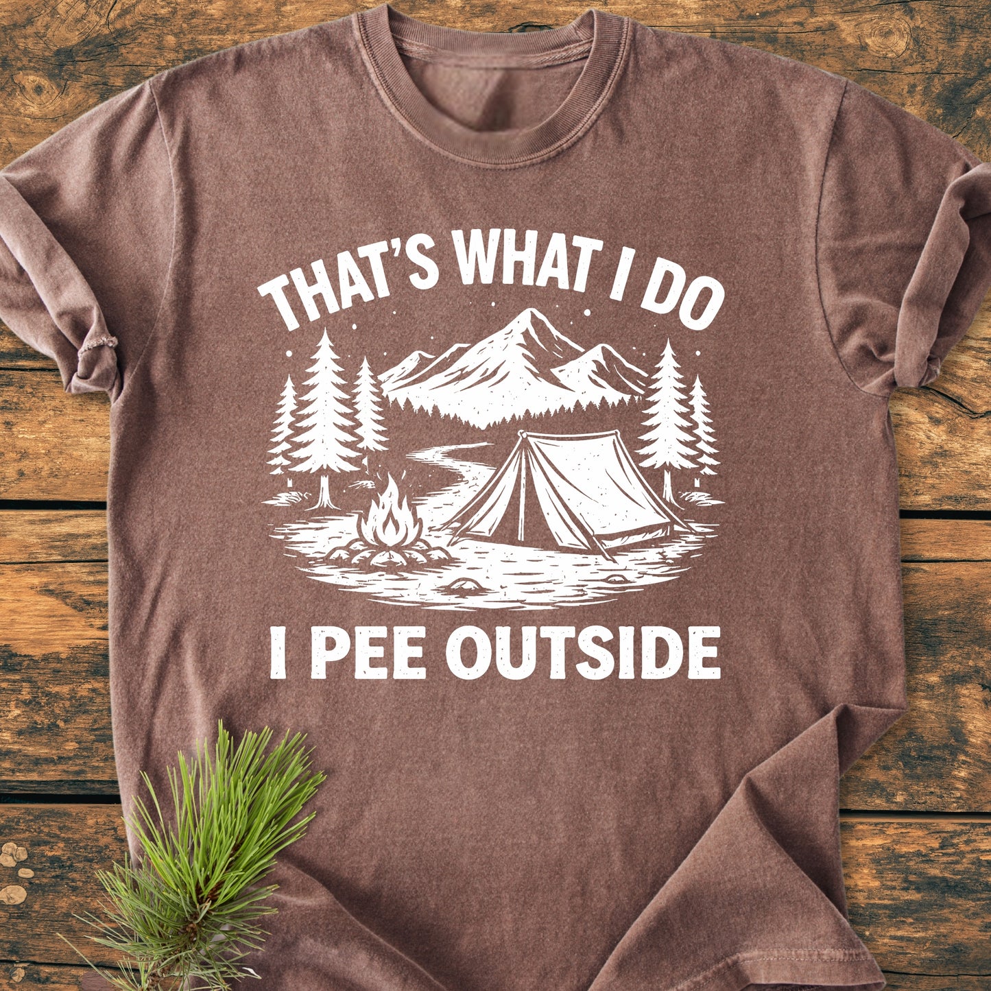 I Pee Outside - Vintage Wash Tee with stylized camping scene, featuring mountains, trees, a tent, and campfire, on soft, garment-dyed 100% cotton, laid flat on wooden surface.
