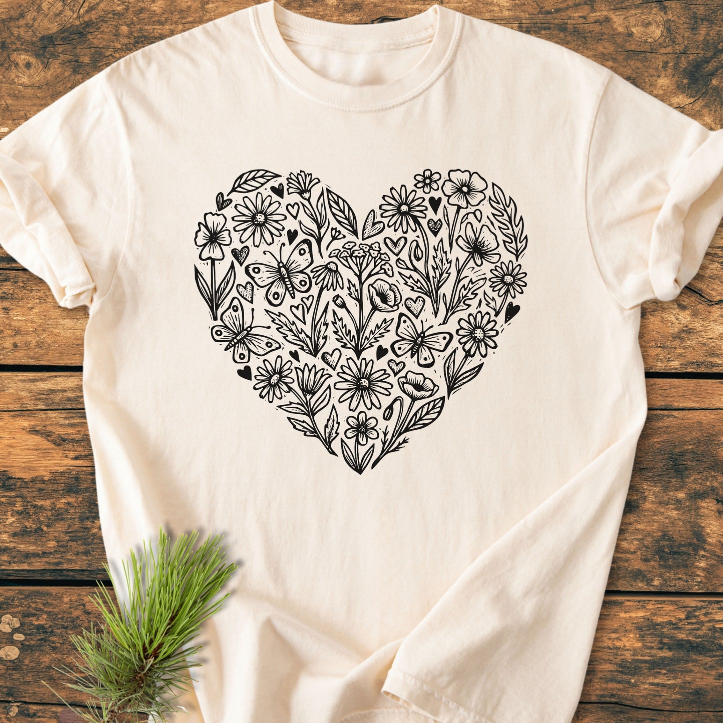 Wildflower Heart Butterfly Soul - Vintage Heavyweight Tee featuring a large doodle-style heart of flowers and butterflies on a light-cream, short-sleeve T-shirt, laid on a rustic wooden surface.