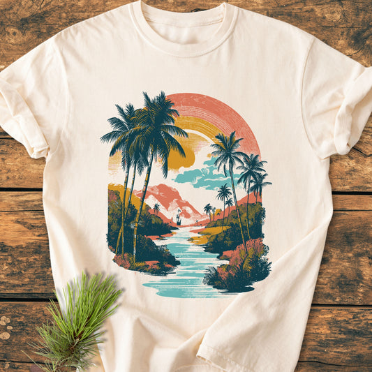 Along The River - Vintage Wash Tee features a vintage tropical scene with palm trees and a sunset. Laid-flat on wood, it highlights Comfort Colors' soft-washed, pre-shrunk, ring-spun cotton.