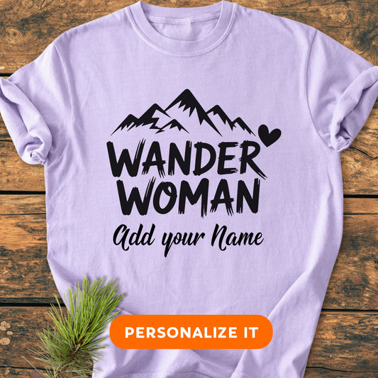 Lavender T-shirt labeled WANDER WOMAN with mountain graphic, customizable Add your Name option, and PERSONALIZE IT button, laid on wood with pine sprig, embodying the Wander Woman | Custom Name | Vintage Wash Tee.