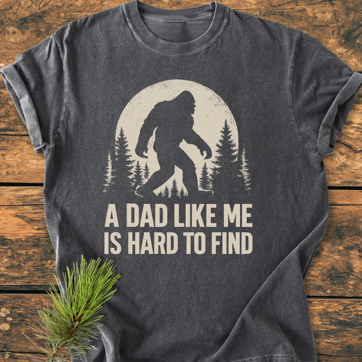 Vintage Bigfoot Dad - Vintage Wash Tee features a stylized Bigfoot graphic with a moon and pine trees, slogan “A DAD LIKE ME IS HARD TO FIND,” on a dark-gray, soft-washed, garment-dyed t-shirt.