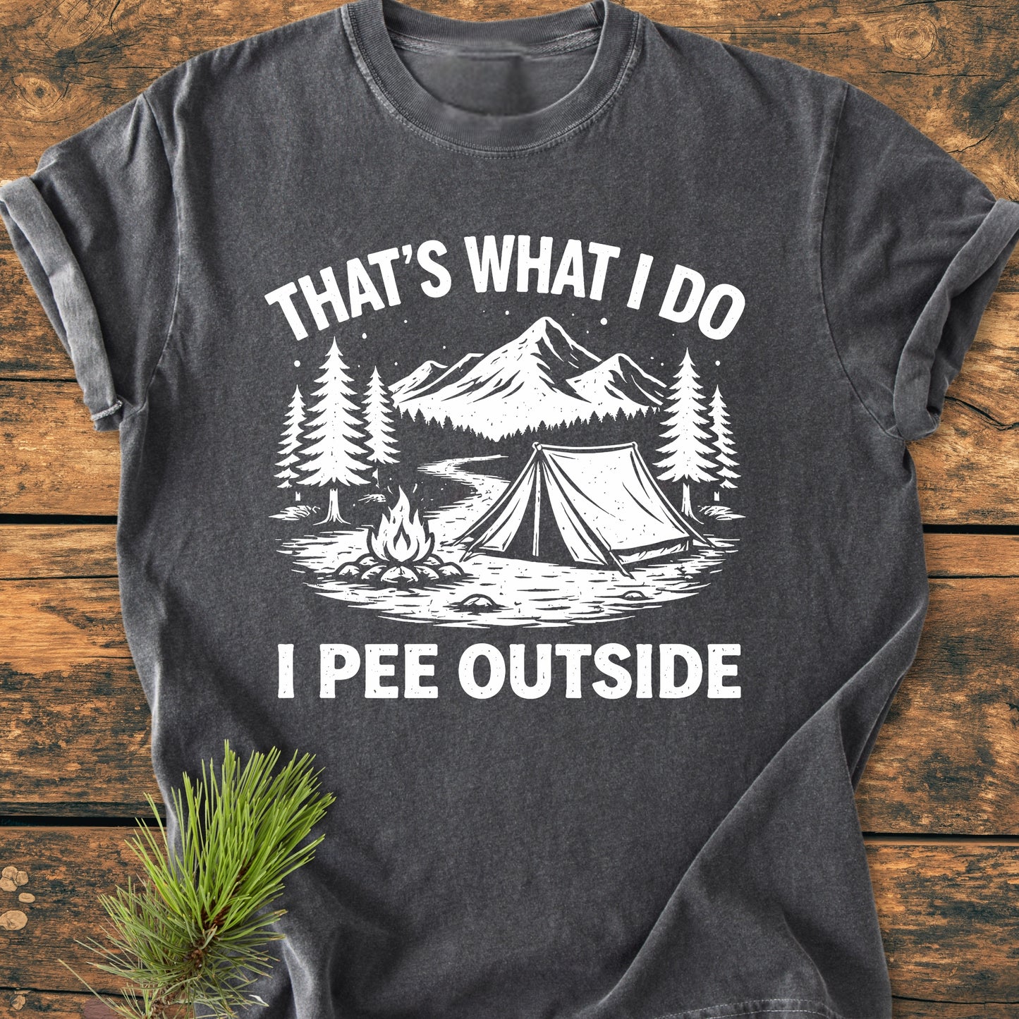 I Pee Outside - Vintage Wash Tee: Dark-gray T-shirt featuring a white ink outdoor scene with pine trees, campfire, tent, stream, and mountains. Text above reads THAT’S WHAT I DO, below says I PEE OUTSIDE.