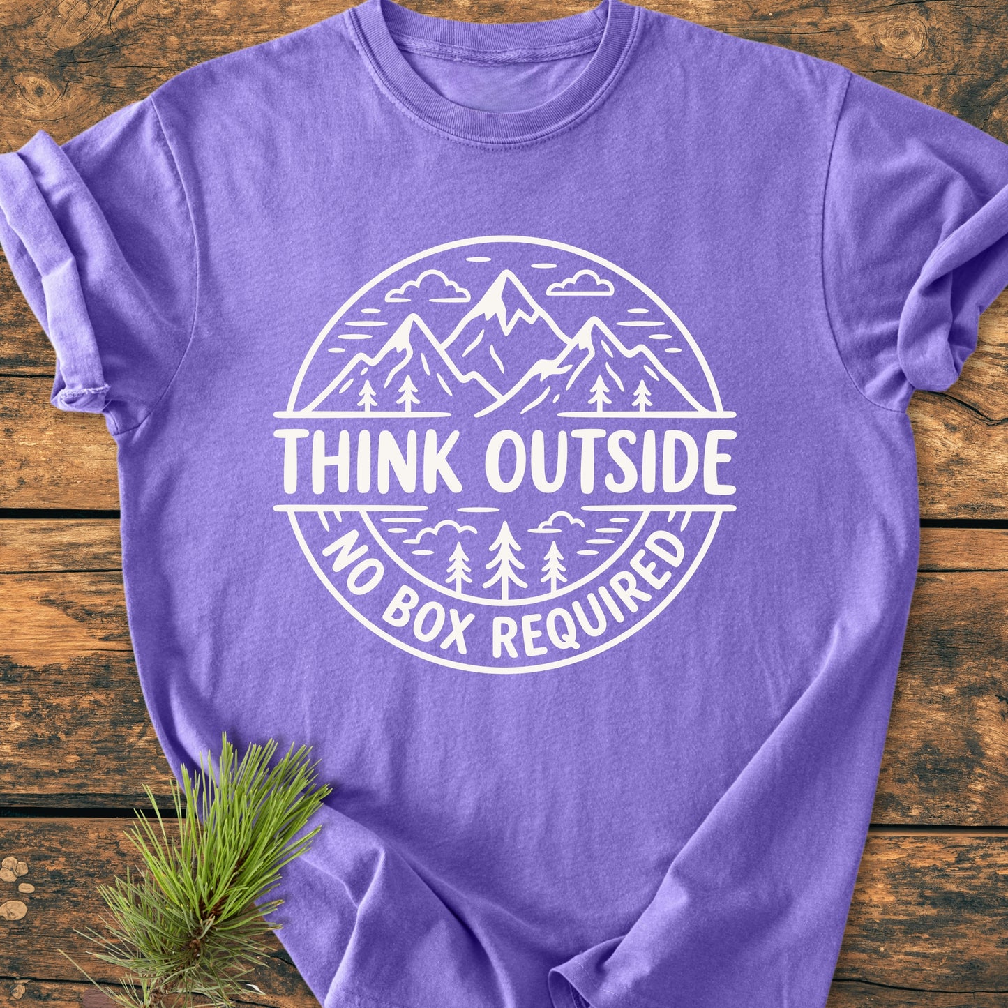 Think Outside - Vintage Wash Tee: Lavender T-shirt with white outdoorsy logo, featuring mountains and trees, laid flat on wood. Includes pine sprig accent, highlighting rustic style.