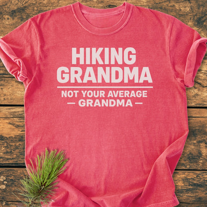 Hiking Grandma - Vintage Wash Tee: A red short-sleeved T-shirt with HIKING GRANDMA in white letters, styled with a pine sprig, showcasing a relaxed fit and durable stitching on a wooden surface.