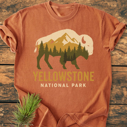 Yellowstone Bison - Vintage Wash Tee: Rust-orange T-shirt featuring a bison graphic with mountain peaks and trees, text YELLOWSTONE NATIONAL PARK, laid on wood with pine sprig, showcasing a cozy, relaxed fit.