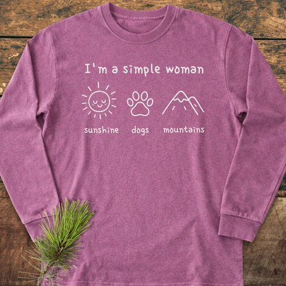 I'm A Simple Woman - Sunshine, Dogs, Mountains Long-Sleeve Tee featuring white text and icons on a heathered shirt, laid on wood with a pine branch. Cozy, 100% ring-spun cotton, classic fit.