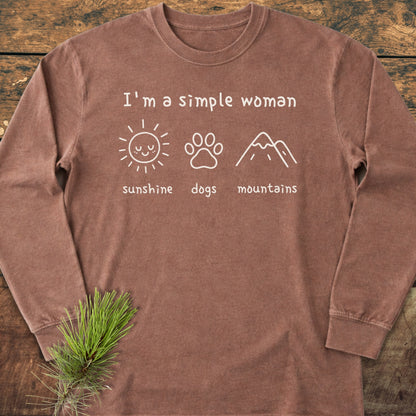 I'm A Simple Woman - Sunshine, Dogs, Mountains Long-Sleeve Tee displayed flat on wood, featuring a soft brown fabric with three white icons—sun, dog paw, and mountain—emphasizing casual comfort and style.