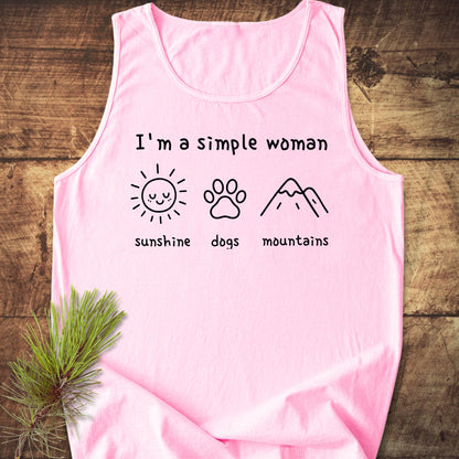 I'm A Simple Woman - Sunshine, Dogs, Mountains Tank Top features a soft pink, sleeveless design with I'm a simple woman and icons of a sun, dog paw-print, and mountains on a wooden surface.
