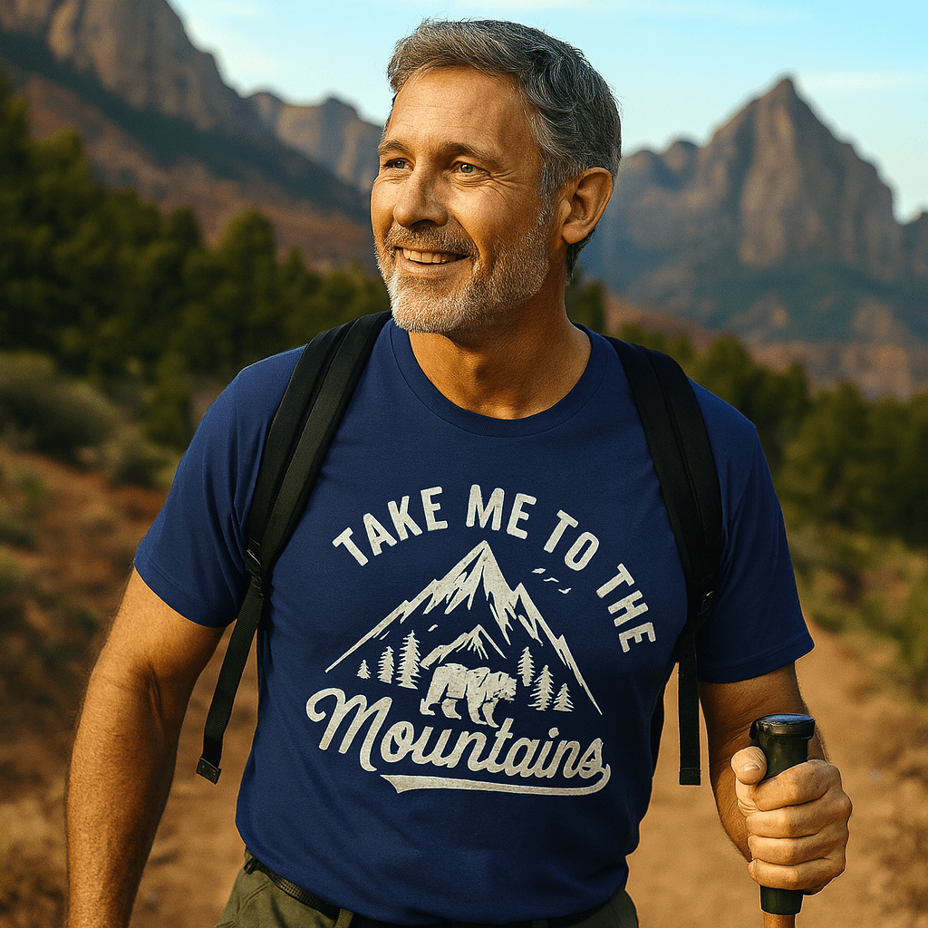 Middle-aged man hiking in a rugged landscape, wearing a Take Me To The Mountains navy T-shirt, black backpack, and holding a trekking pole.