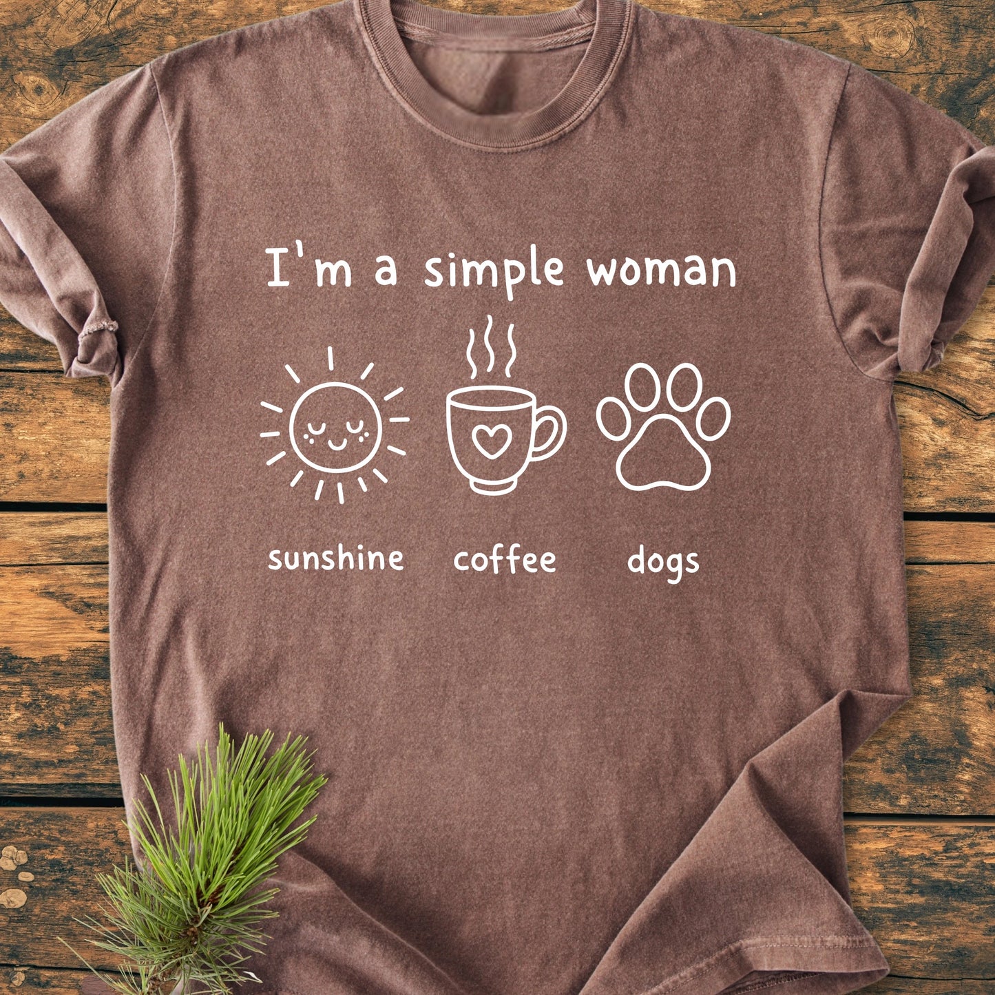 I'm A Simple Woman. Sunshine Coffee Dogs - Vintage Wash Tee with white text and cute icons on a brown T-shirt, laid flat on a wooden surface.