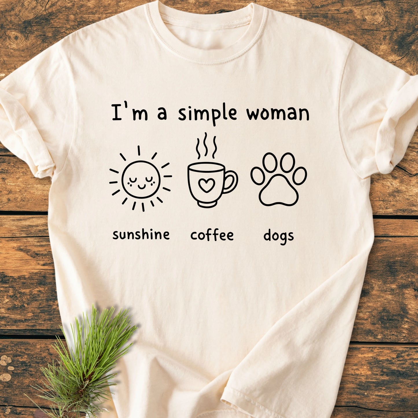 I'm A Simple Woman. Sunshine Coffee Dogs - Vintage Wash Tee on a wooden surface, featuring icons of a sun, coffee mug, and dog paw, embodying simple, joyful living for dog and coffee lovers.