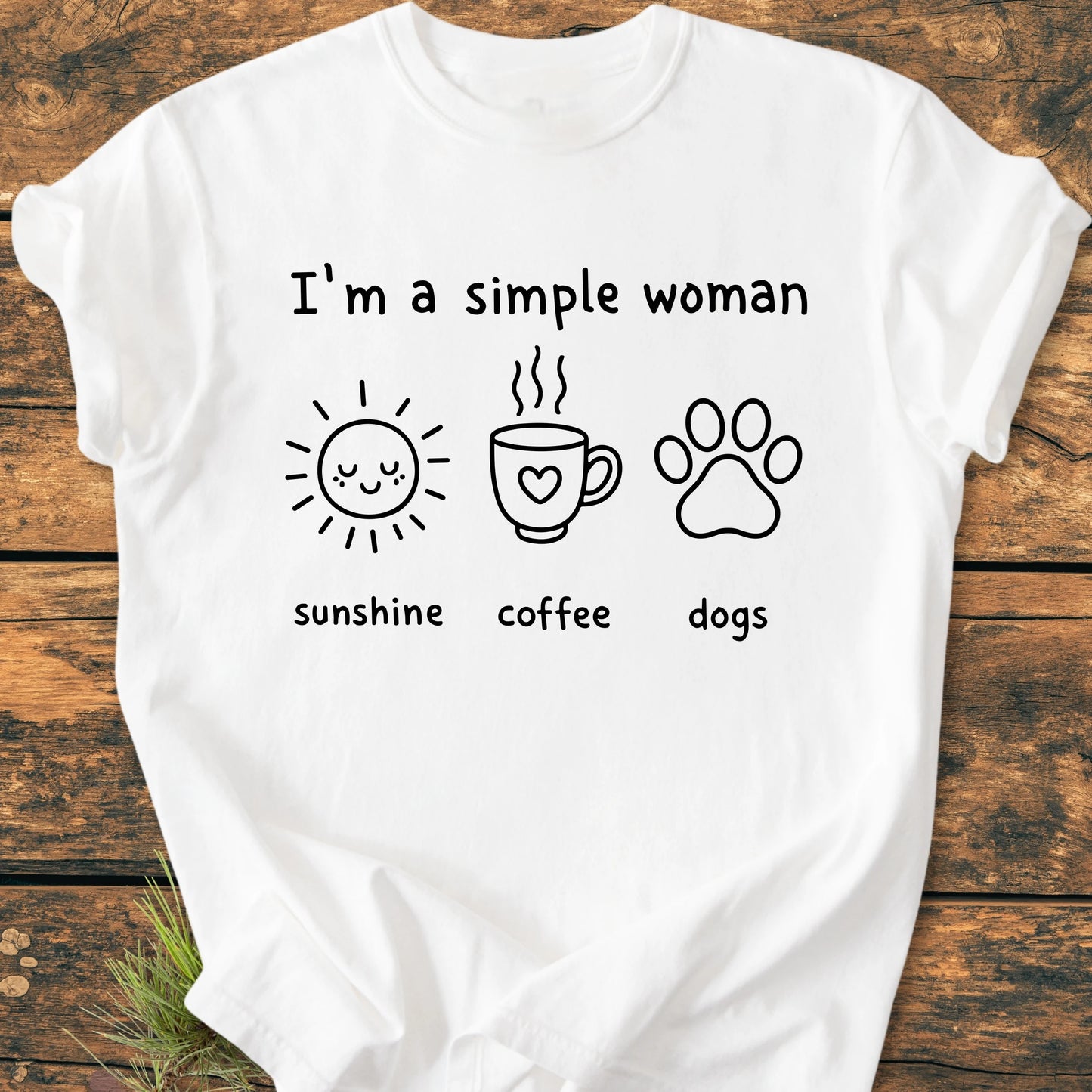I'm A Simple Woman. Sunshine Coffee Dogs - Vintage Wash Tee features charming icons of a sun, coffee cup, and dog paw, embodying simple joys, on a rustic wooden surface.