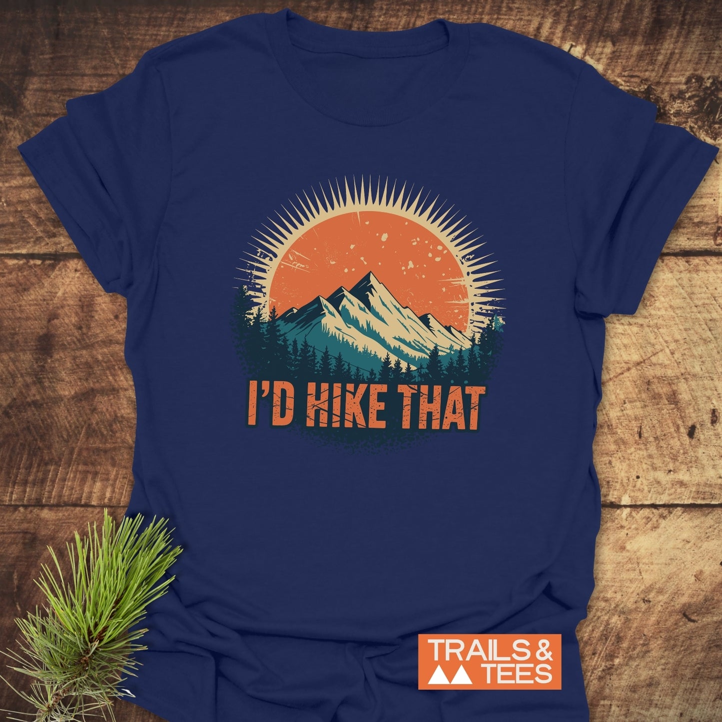 I'd Hike That T-Shirt features a sun and mountains graphic with 'I'D HIKE THAT' slogan. The unisex, soft cotton tee is perfect for adventures, featuring the Trails & Tees logo.