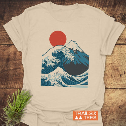 Mountain And Wave T-Shirt featuring a stylized Hokusai-inspired wave, Mount Fuji, and sun graphic. Displayed on wood with TRAILS & TEES label; embodies adventure-ready comfort and design.