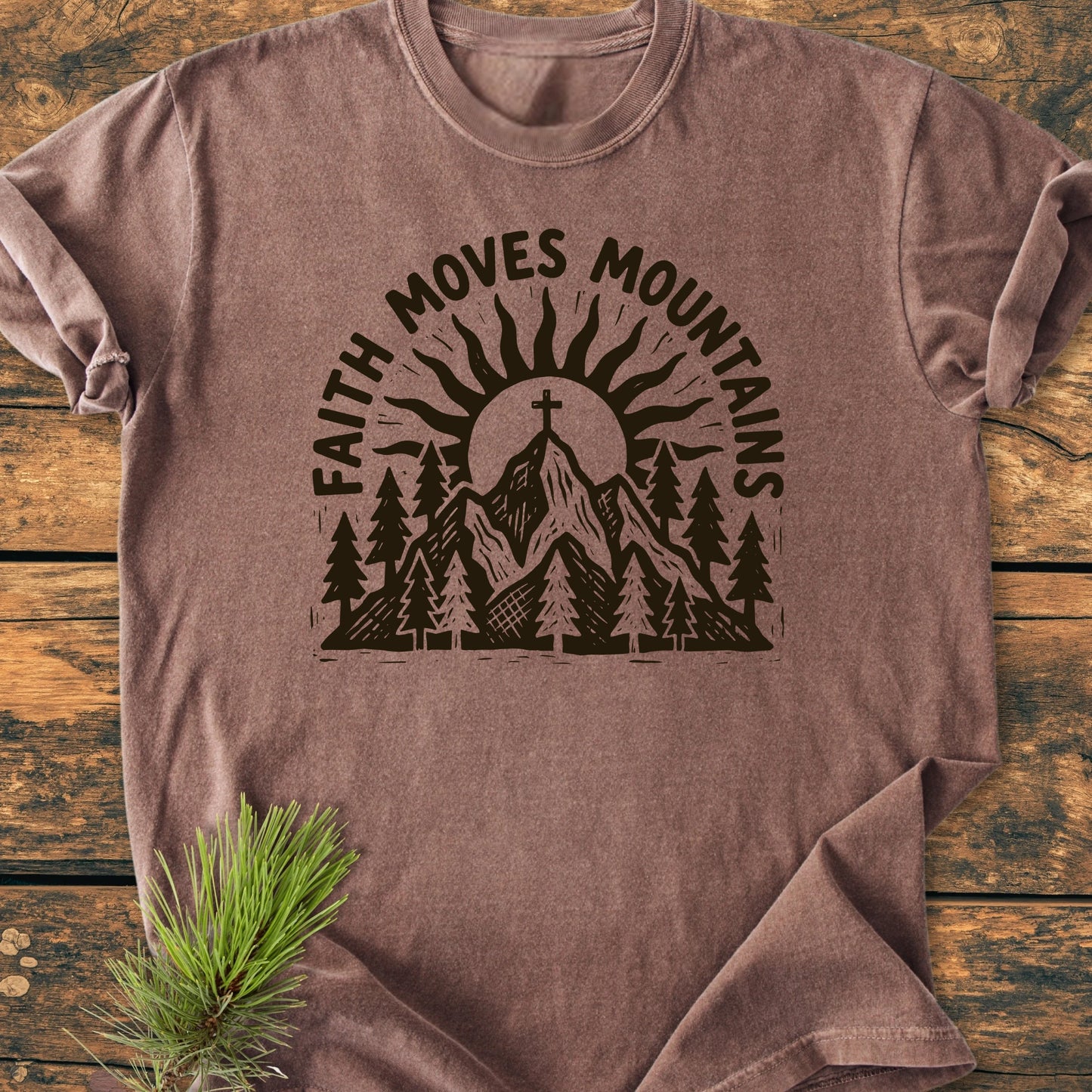 1409 Faith Moves Mountains T-shirt featuring a bold mountain and cross graphic, laid on wood, with 'FAITH MOVES MOUNTAINS' text, emphasizing its rustic, outdoorsy appeal and relaxed fit.