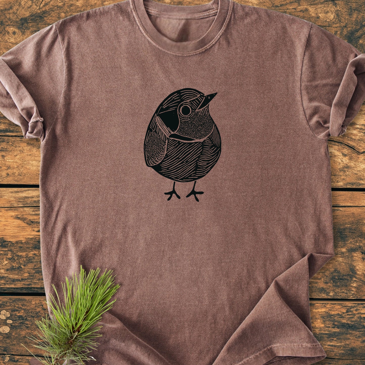 1433 Little Robin T-shirt features a stylized bird illustration on a soft, vintage wash tee. Laid flat with rolled sleeves, it embodies comfort and a relaxed fit for everyday wear.