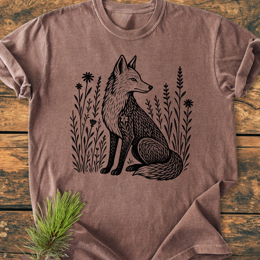 The 225 Wildflower Fox DARK T-shirt features a black fox illustration surrounded by wildflowers on a brown, short-sleeve tee, displayed on a wooden surface with a pine sprig accent.