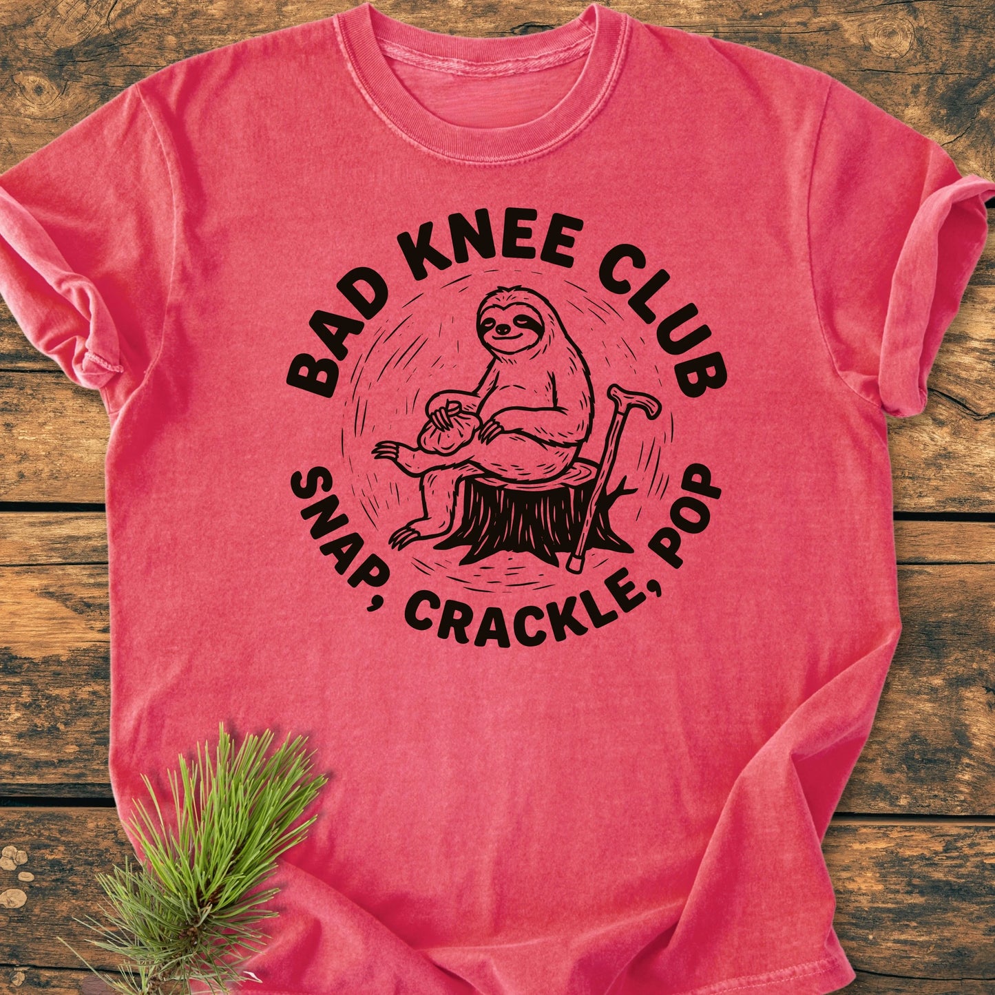 Heathered pink T-shirt with BAD KNEE CLUB design, featuring a sloth on a stump with a cane. Soft, vintage wash, relaxed fit, and durable for everyday adventures.