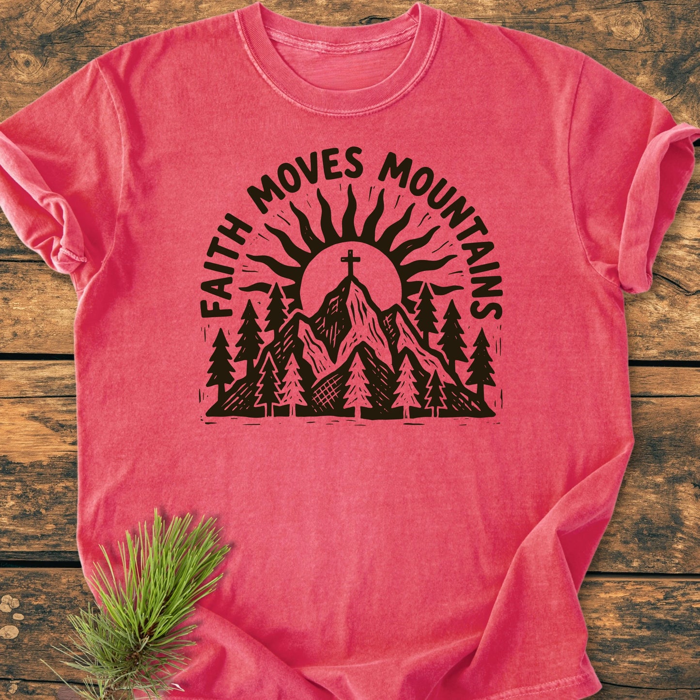 The 1409 Faith Moves Mountains T-shirt features a mountain scene with a cross and rising sun, framed by the phrase, Faith Moves Mountains, displayed on a soft, relaxed-fit shirt.