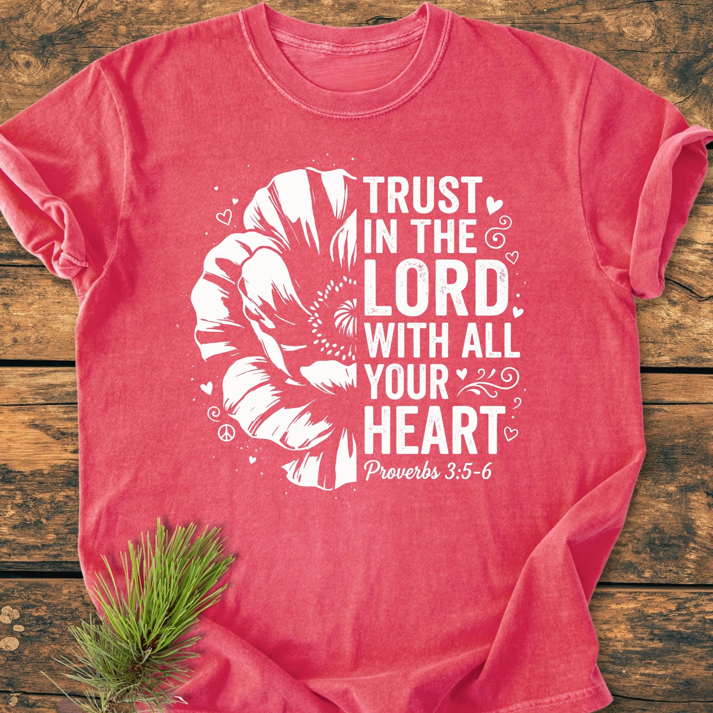 Trust In The Lord - Vintage Wash Tee features a large stylized flower and text from Proverbs 3:5–6, screen-printed on a soft, relaxed-fit T-shirt laid on a rustic wooden surface.